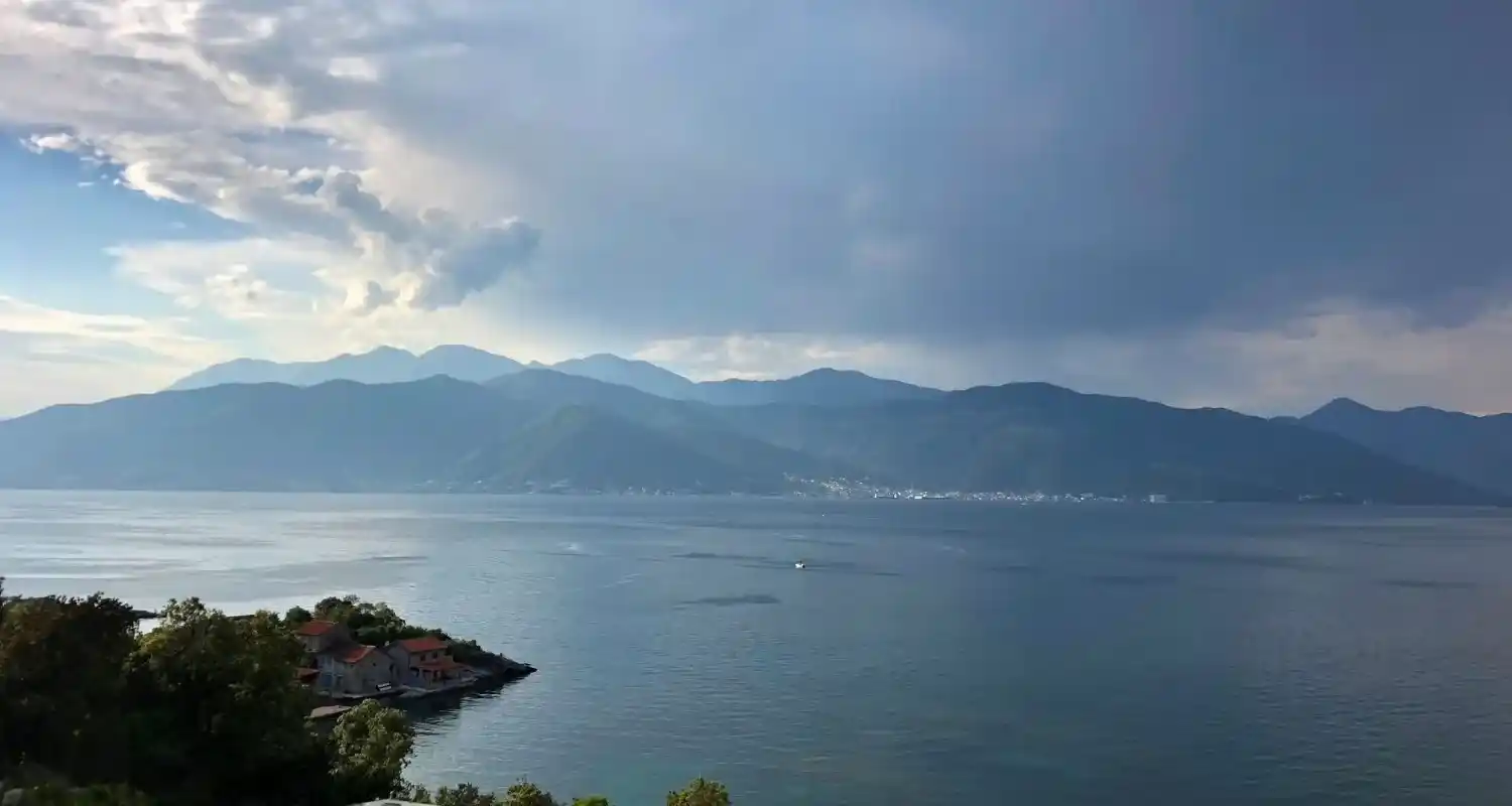 Boka Kotorska pod dramatičnim oblacima, okružena planinama i zelenom obalom poluostrva Luštica