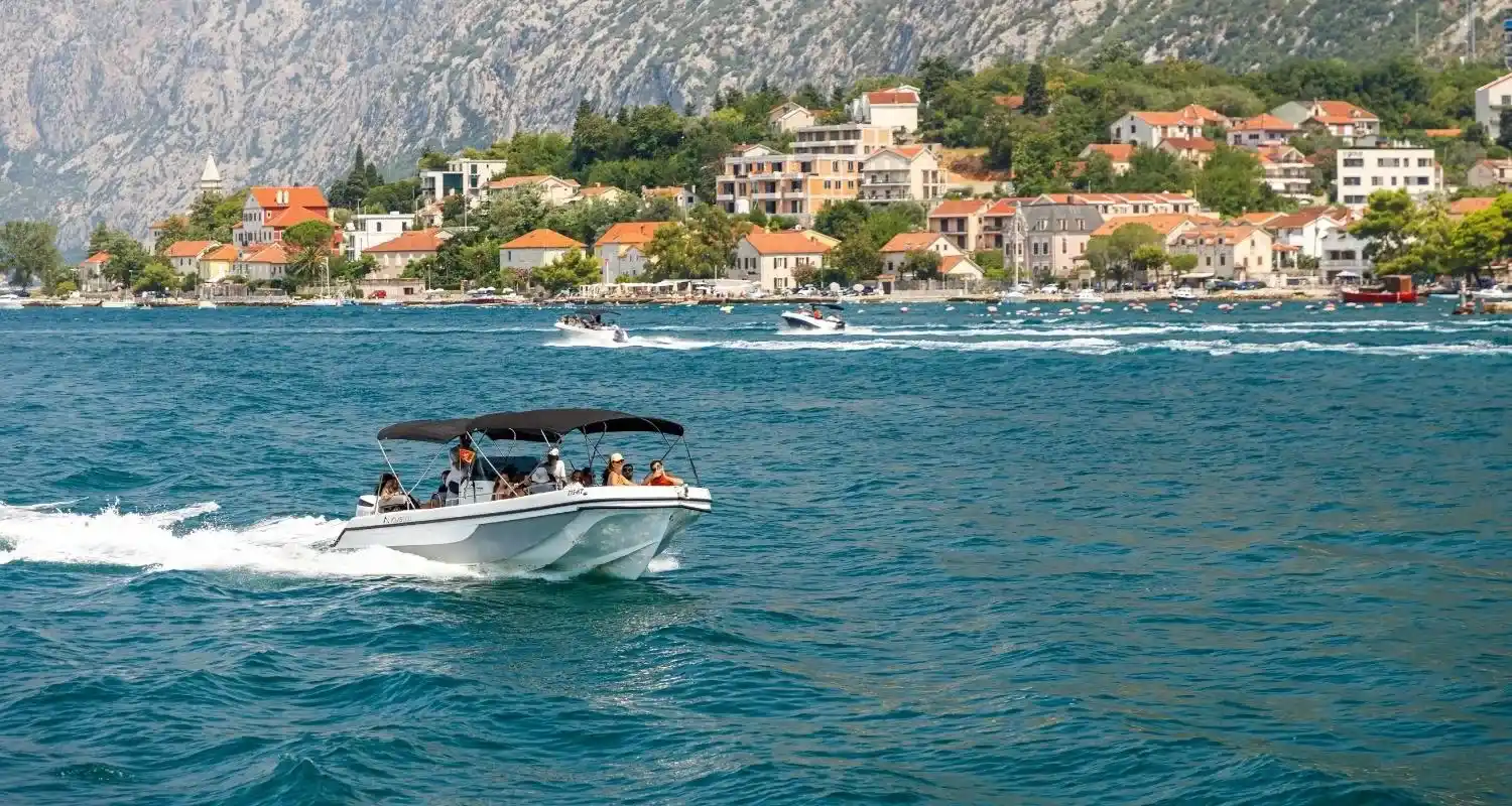 Gliser sa putnicima plovi Bokom Kotorskom u blizini poluostrva Luštica, uz primorsko naselje i strme planine