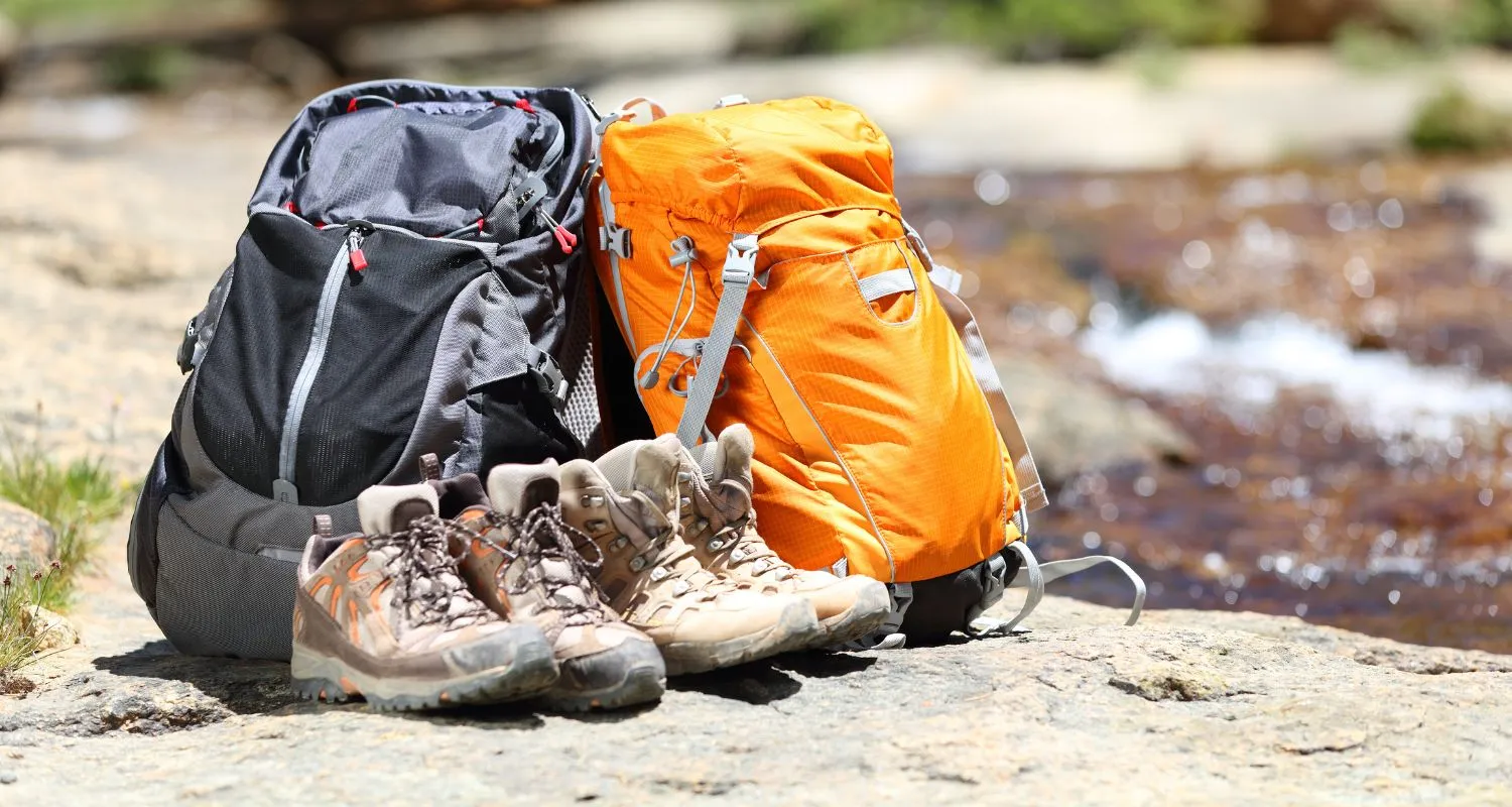Hiking backpacks and boots resting on a rock beside a mountain stream