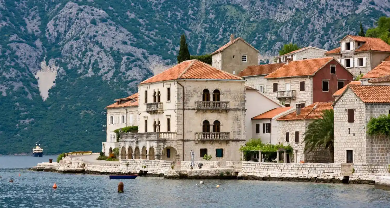 Stone palaces in Perast by the sea, with red rooftops and the mountains of the Bay of Kotor in the background