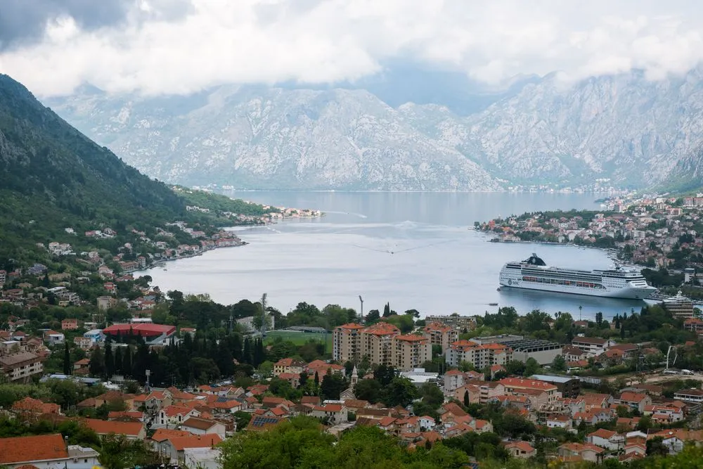 Pogled na Kotor, kruzer u Bokokotorskom zalivu i planine pod oblacima.