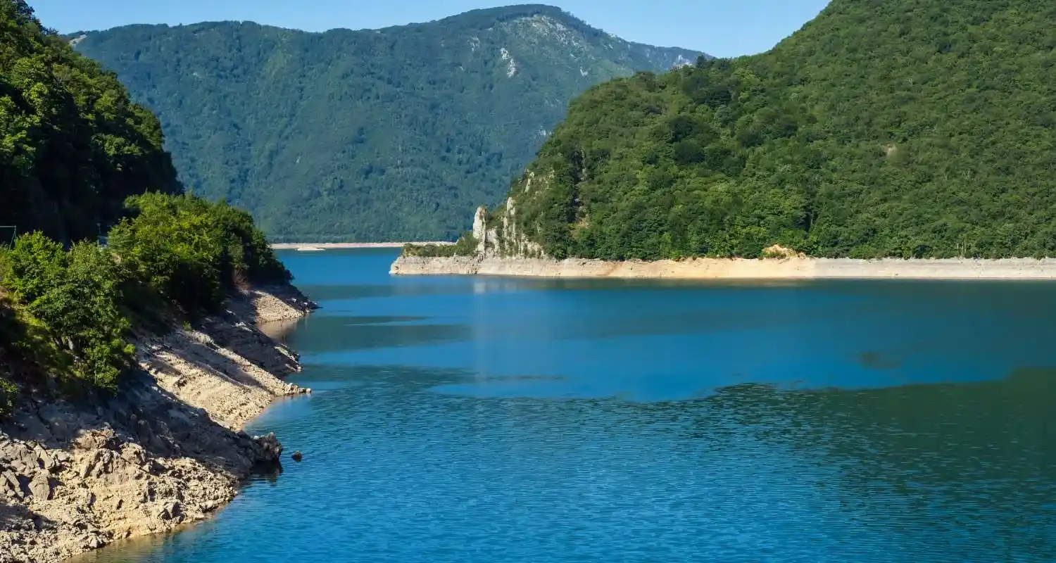 Calm shore of Piva Lake with blue water, rocky edges and green mountains