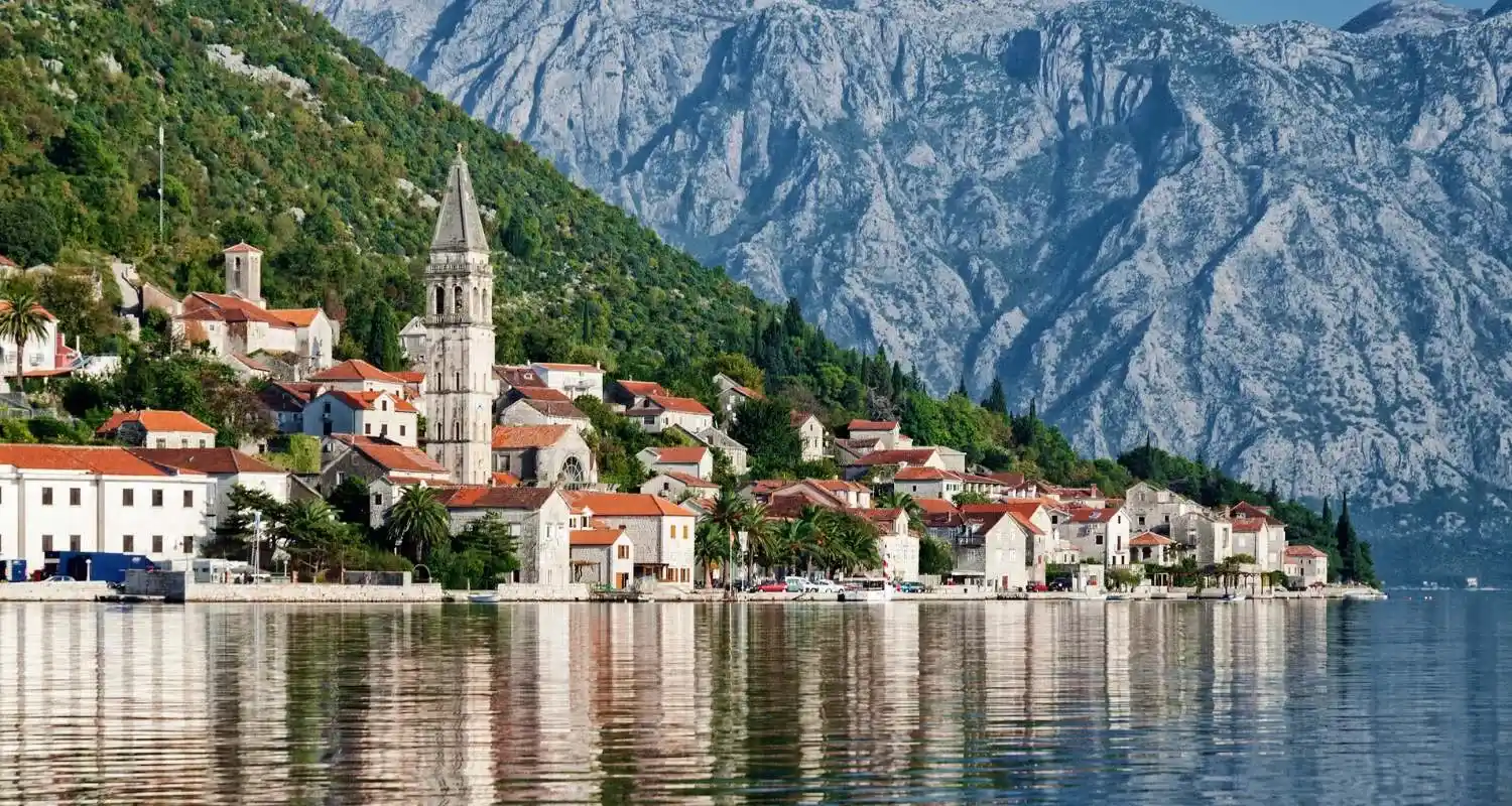 Perast on the Bay of Kotor coast with a church bell tower, stone houses, and mountains in the background