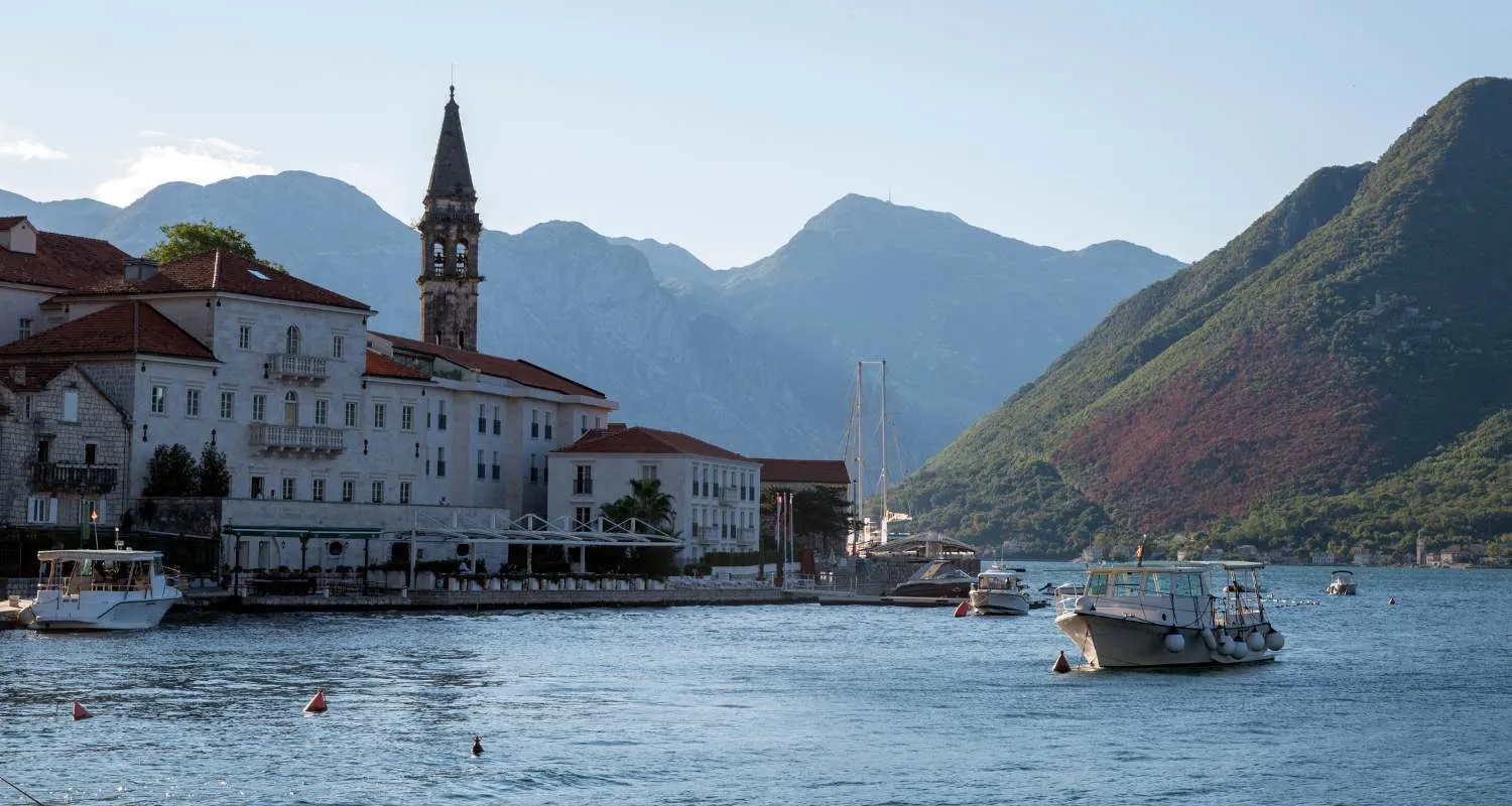 Perast on the shore of the Bay of Kotor with boats, a church bell tower, and mountains in the background