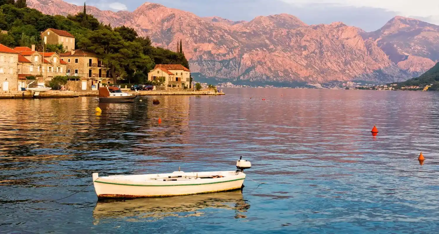 Calm bay near Perast with a small boat on the water, stone houses, and mountains in the background