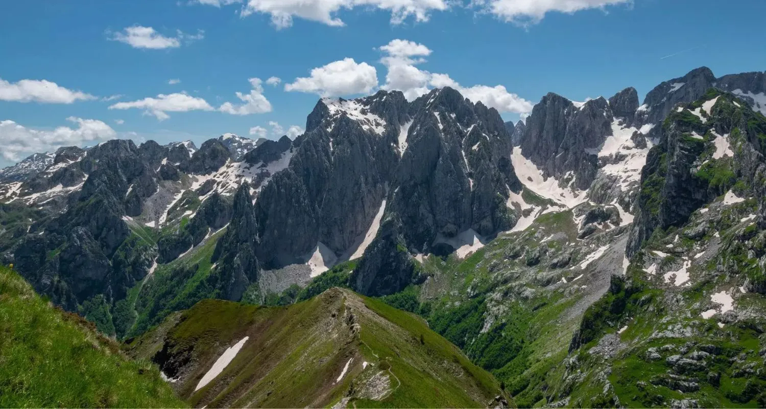 Snow-filled gullies on rocky peaks above a green mountain ridge