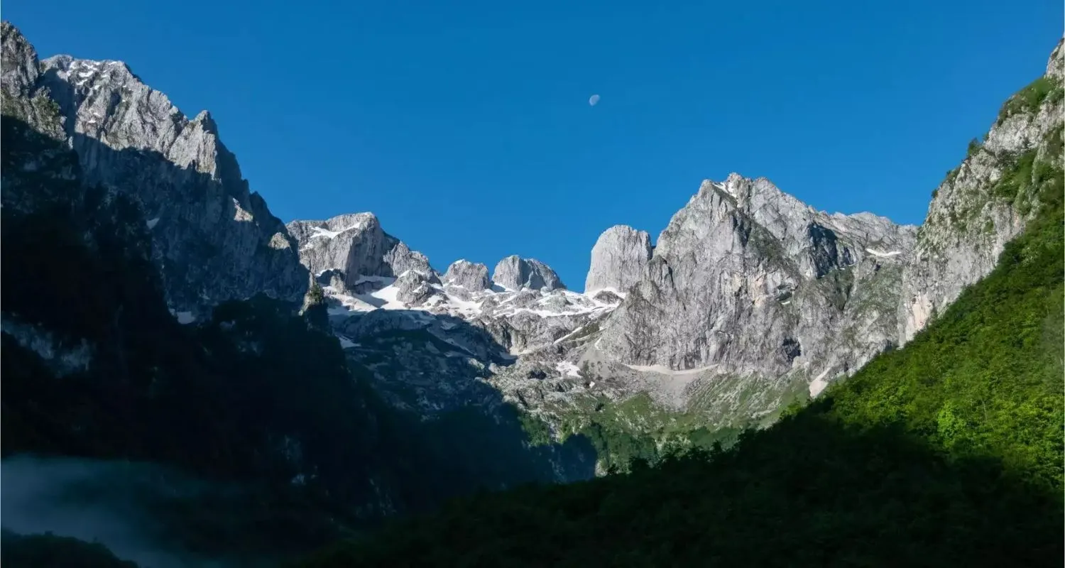 Jagged peaks of Prokletije National Park rising above a forested mountain valley