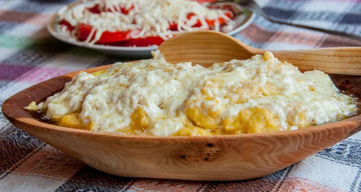 Traditional kačamak served in a wooden bowl with cheese and kajmak