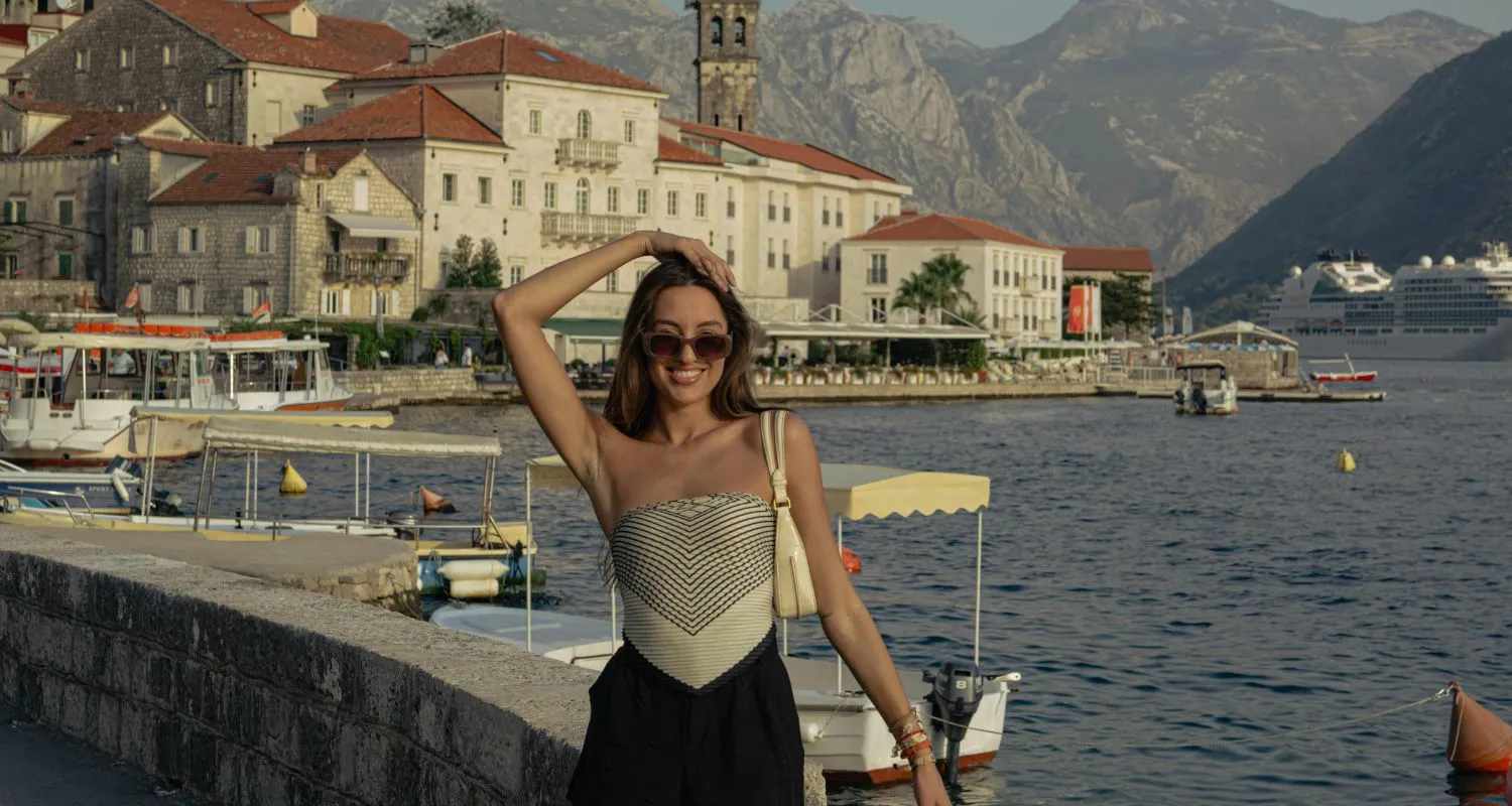 Turistkinja na obali Boke Kotorske tokom putovanja u Crnu Goru, sa starim gradom Perastom u pozadini
