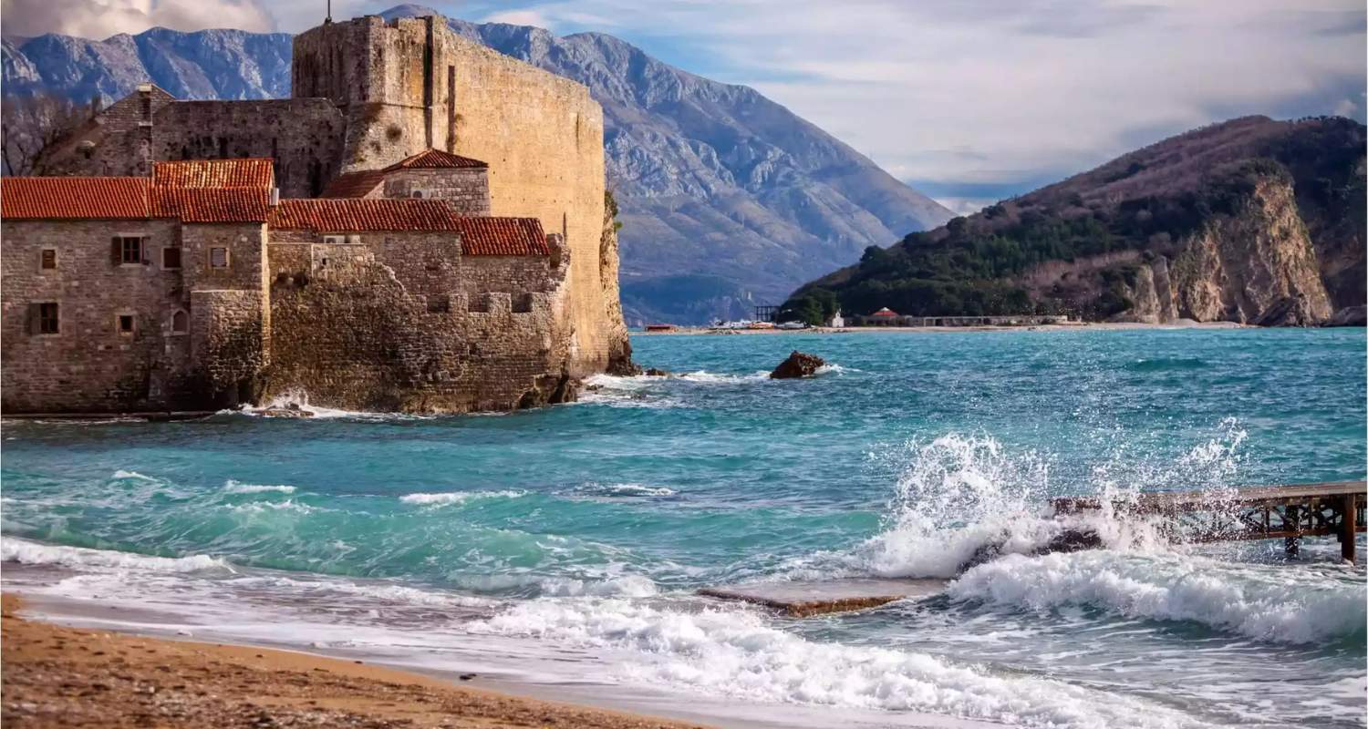 Waves crashing near the walls of Budva Old Town with mountains in the background