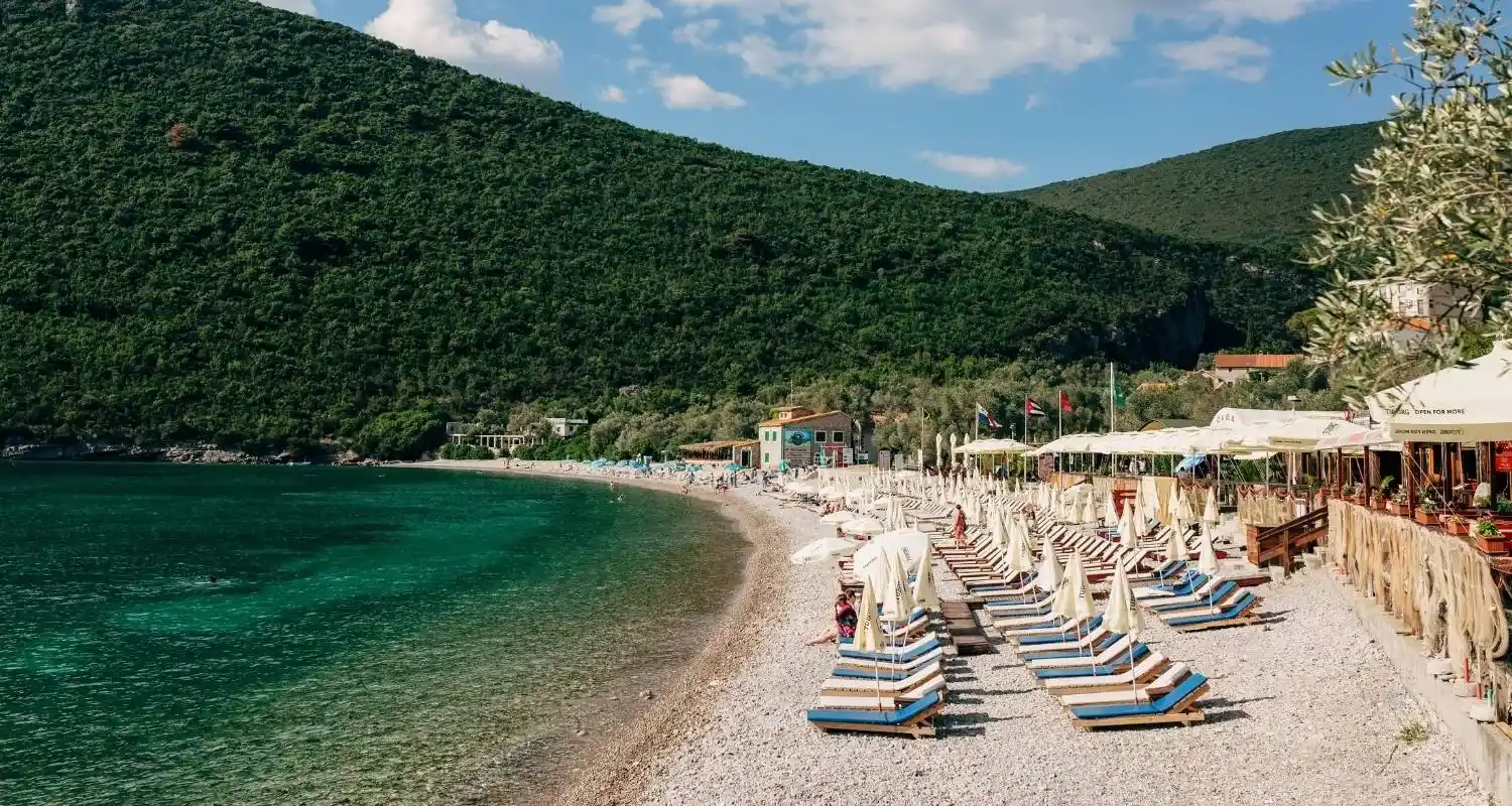 Plaža Žanjice na poluostrvu Luštica sa tirkiznim morem, šljunkovitom obalom i uredno postavljenim ležaljkama